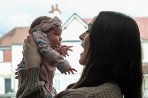 A mum lifting up a very small baby and pulling a fun face