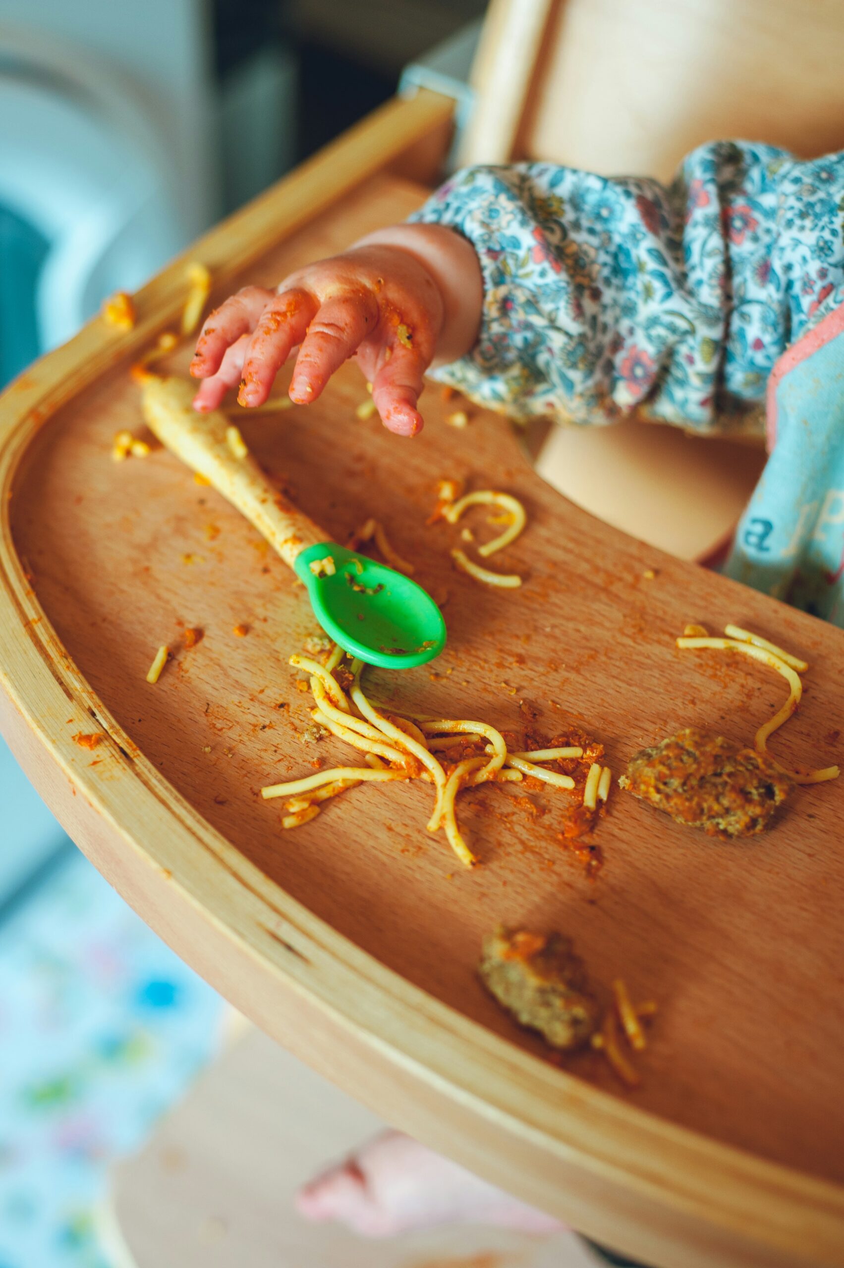 A messy high chair that's covered in spaghetti and sauce for baby weaning