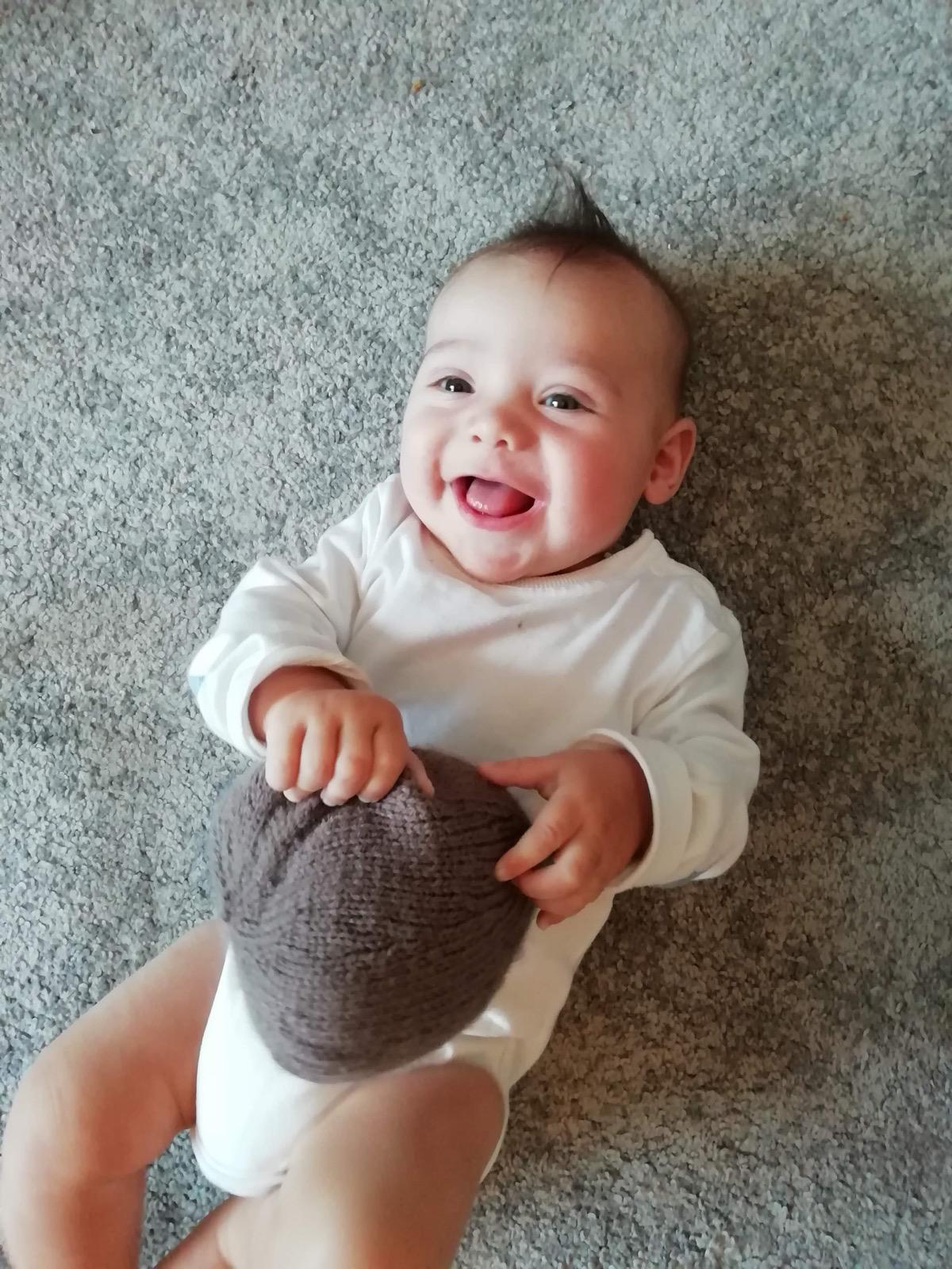 A baby with dark spiky hair holding onto a knitted boob used for demonstrations